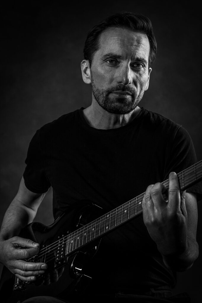 Stoere lowkey portretfoto in zwartwit van een man met gitaar.